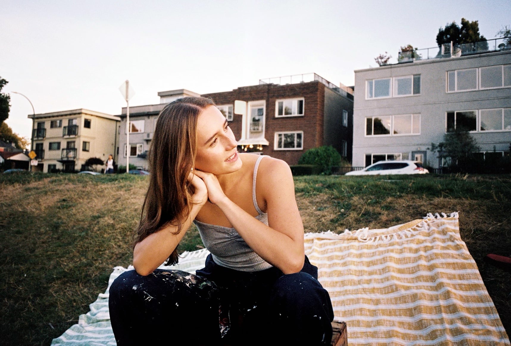 Ella Thomas sitting on picnic blankets in a Vancouver park at dusk, wearing paint-splattered trousers