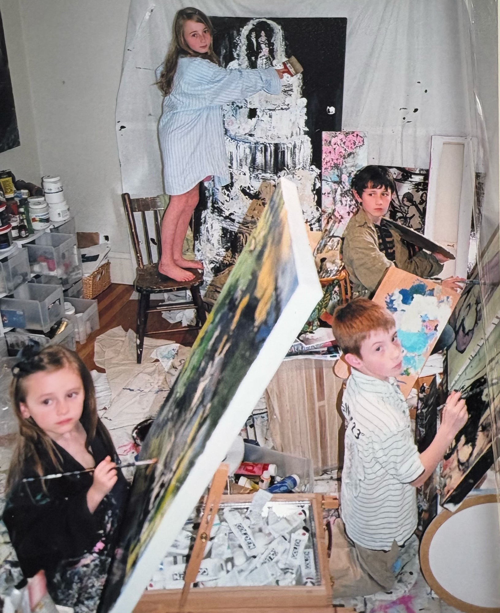 Ella and other children painting on canvases in a crowded home studio